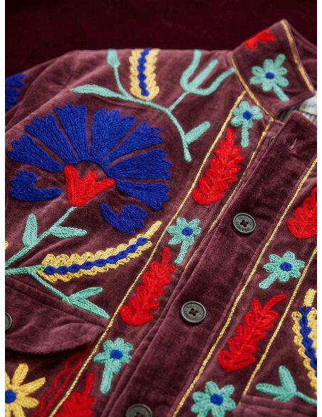Pormenor em close-up dos bordados florais coloridos e botões do casaco em veludo bordeaux